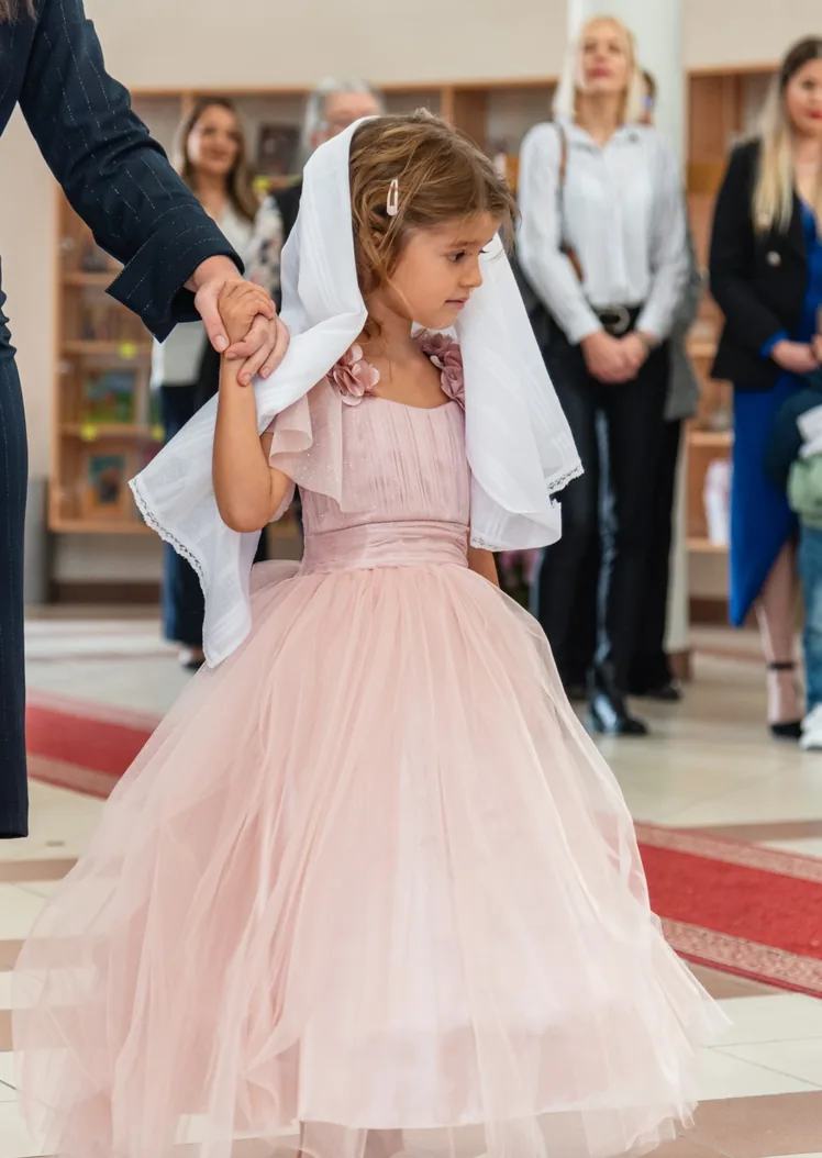 Devojčica u roze haljini sa belom maramom tokom krštenja